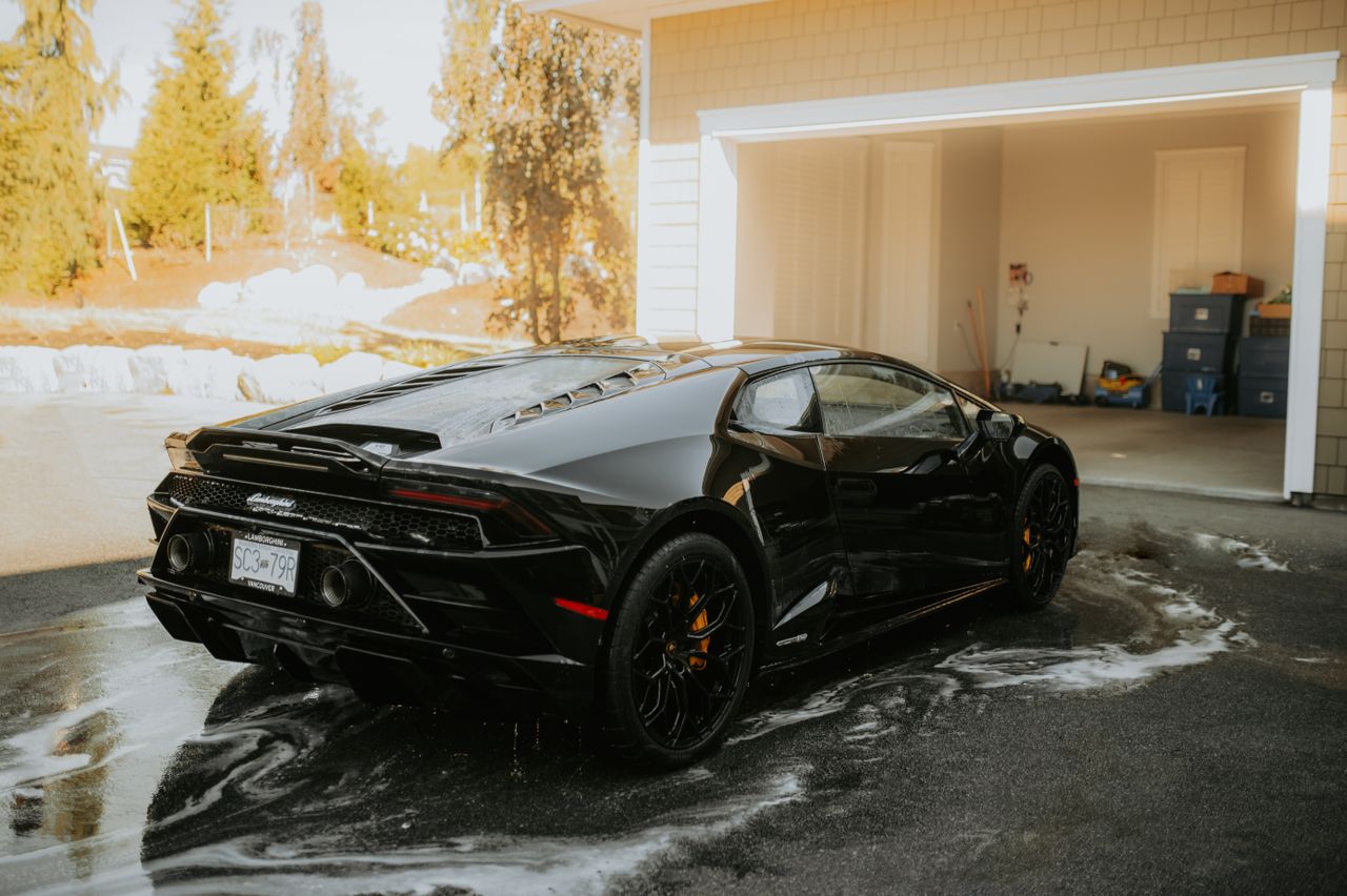 High-end Lamborghini sports car being washed at a sunny outdoor location.